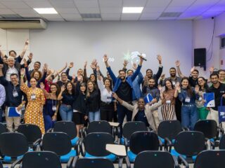 Participantes do Momento Negócio de agosto reunidos no auditório da Faculdade Estácio de Sá, em Jardim Camburi, com os braços erguidos e sacolas da CDL Vitória