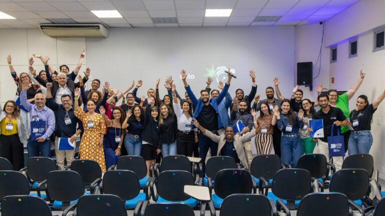 Participantes do Momento Negócio de agosto reunidos no auditório da Faculdade Estácio de Sá, em Jardim Camburi, com os braços erguidos e sacolas da CDL Vitória