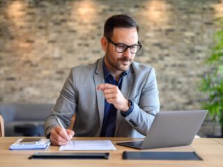 Empresário de terno faz anotações em uma mesa com notebook, analisando opções de plano de saúde para a equipe