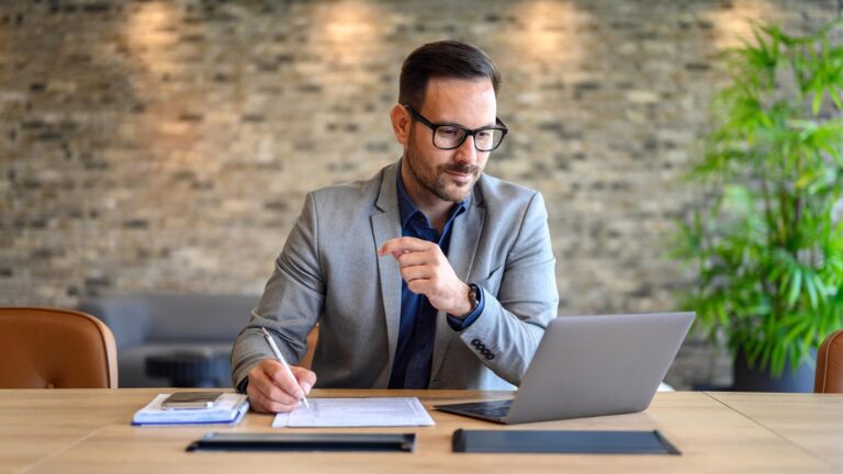 Empresário de terno faz anotações em uma mesa com notebook, analisando opções de plano de saúde para a equipe