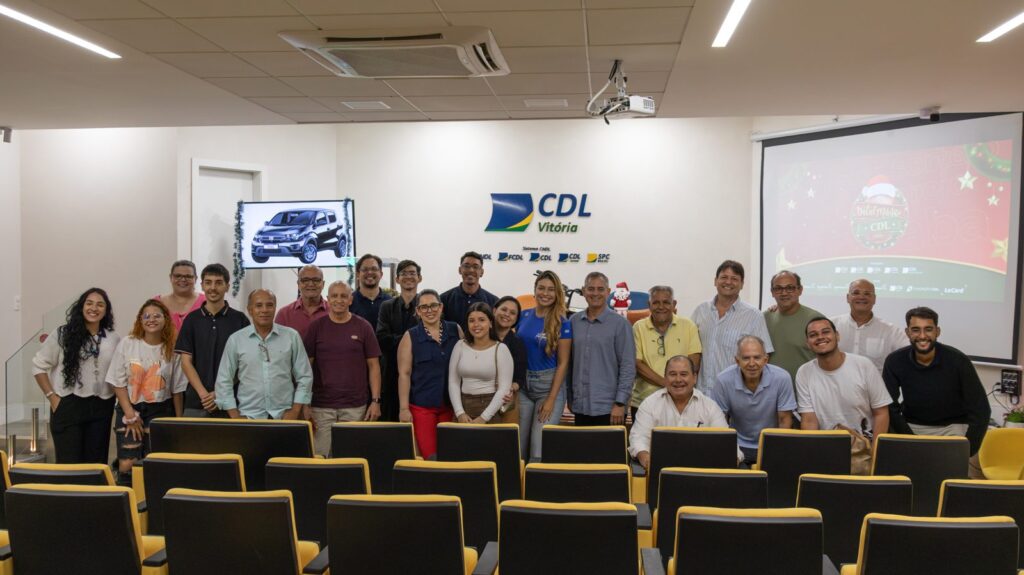 Empresários e equipe da CDL Vitória reunidos na sede da entidade durante o lançamento do Natal Mágico CDL 2026, com o carro zero km do sorteio na TV e a arte da campanha no telão